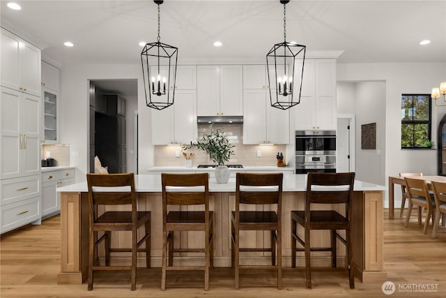 kitchen with under cabinet range hood, double oven, an inviting chandelier, and light countertops