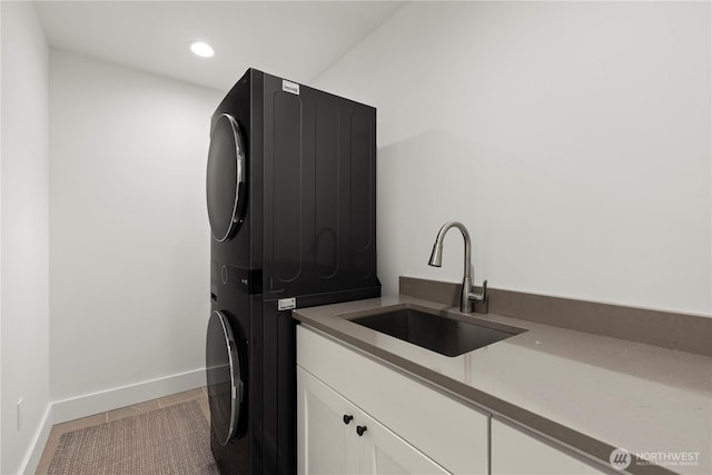 washroom featuring stacked washer and clothes dryer, a sink, recessed lighting, cabinet space, and baseboards