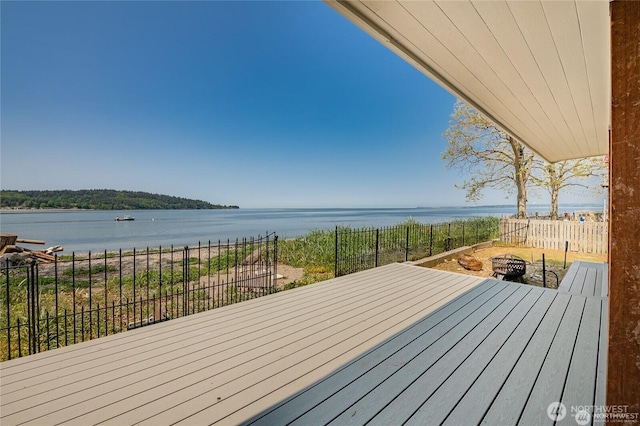 wooden deck with a water view, fence, and an outdoor fire pit