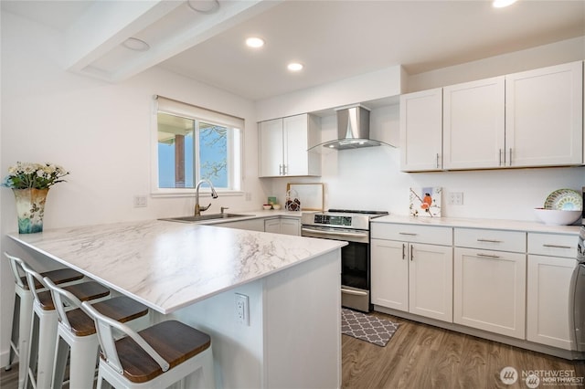 kitchen with electric stove, a sink, a peninsula, a breakfast bar area, and wall chimney exhaust hood