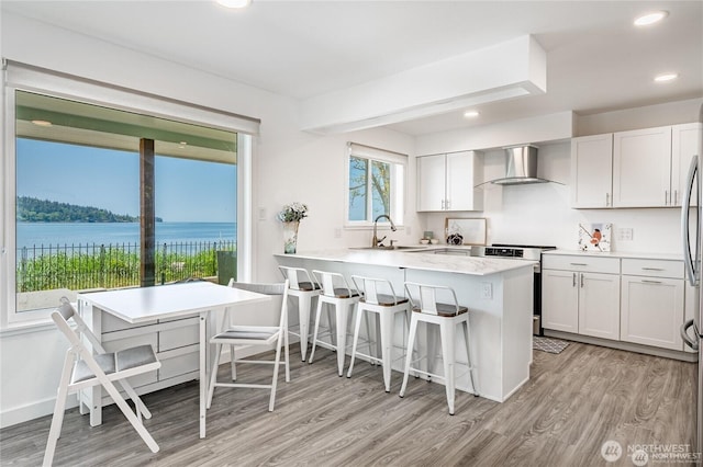 kitchen featuring a peninsula, a sink, stainless steel range with electric cooktop, a kitchen bar, and wall chimney exhaust hood