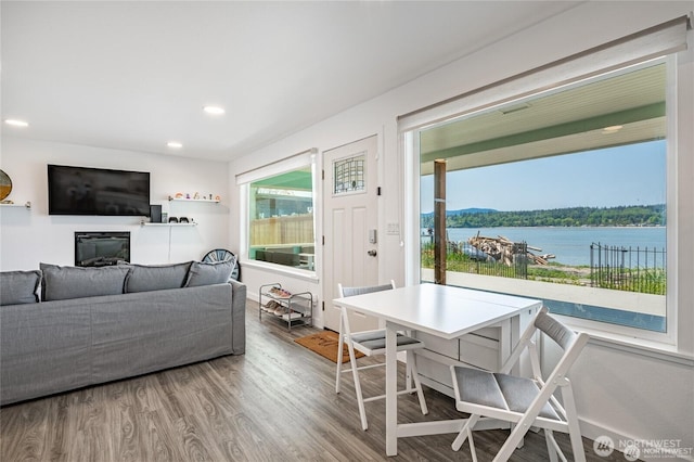 living room featuring a glass covered fireplace, recessed lighting, wood finished floors, and a water view