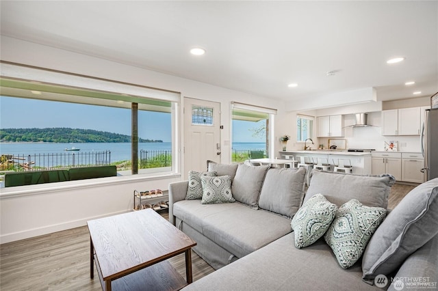 living area featuring recessed lighting, light wood-type flooring, baseboards, and a water view