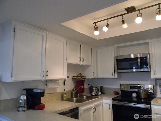 kitchen with light countertops, a tray ceiling, white cabinets, stainless steel appliances, and a sink