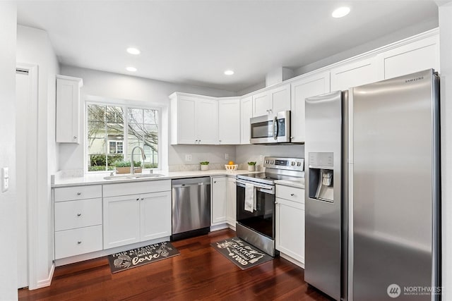 kitchen with a sink, light countertops, white cabinets, dark wood-type flooring, and appliances with stainless steel finishes