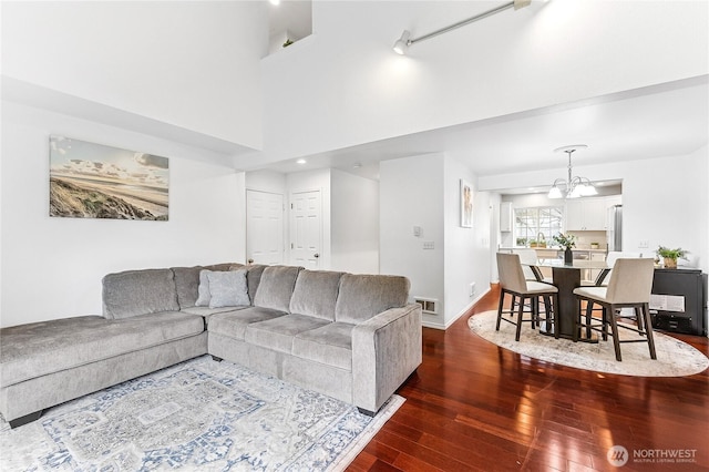 living area featuring visible vents, dark wood-type flooring, baseboards, a high ceiling, and an inviting chandelier