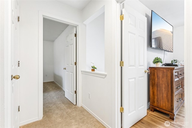 hallway featuring light colored carpet and baseboards