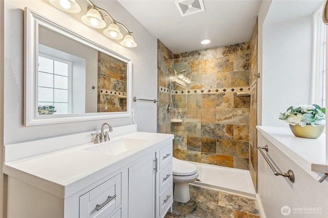 bathroom featuring a tile shower, visible vents, toilet, and vanity