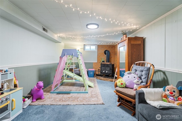 recreation room featuring a wood stove, carpet, and visible vents