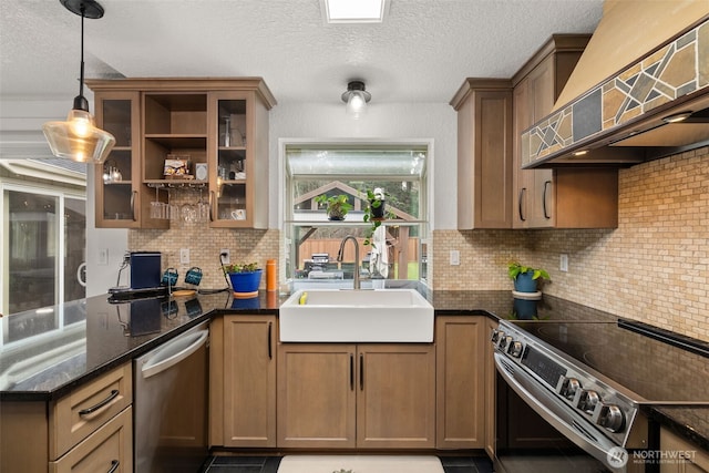 kitchen featuring pendant lighting, a sink, backsplash, stainless steel appliances, and wall chimney exhaust hood