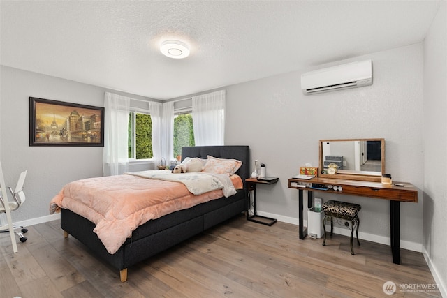 bedroom with a textured ceiling, a wall mounted AC, baseboards, and wood finished floors