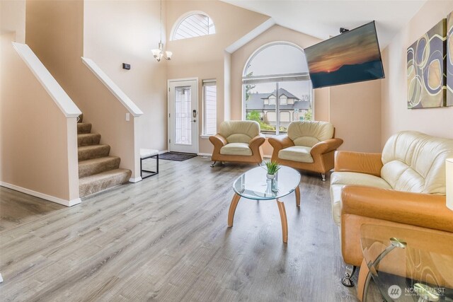 living area with high vaulted ceiling, a healthy amount of sunlight, wood finished floors, and stairs