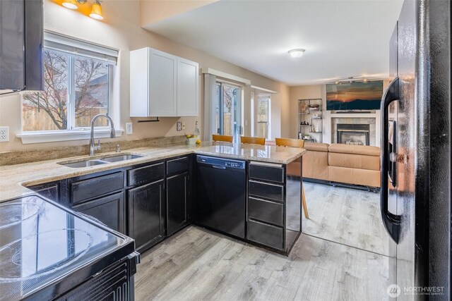 kitchen with a tile fireplace, a sink, black appliances, white cabinets, and light wood-type flooring