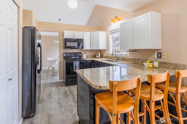 kitchen with black appliances, a sink, a kitchen breakfast bar, a peninsula, and white cabinets