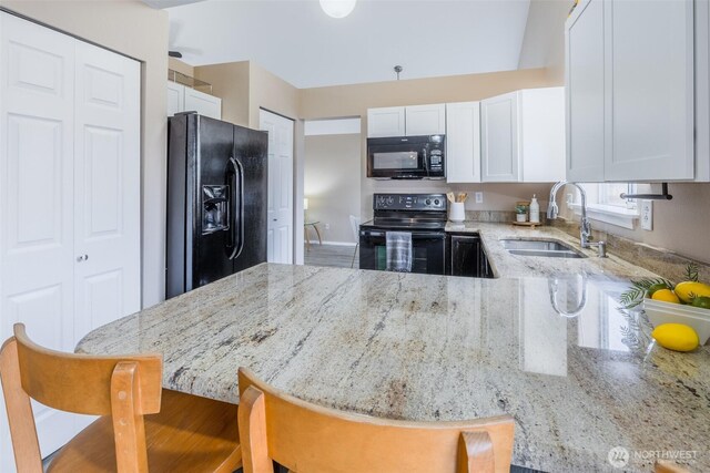 kitchen featuring light stone counters, a peninsula, a sink, black appliances, and white cabinetry