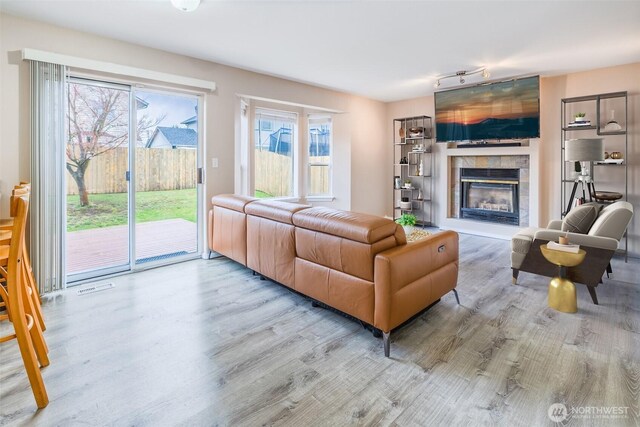 living room with a tiled fireplace, wood finished floors, visible vents, and a healthy amount of sunlight