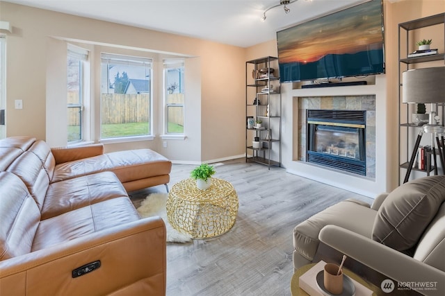 living room featuring baseboards, wood finished floors, and a glass covered fireplace