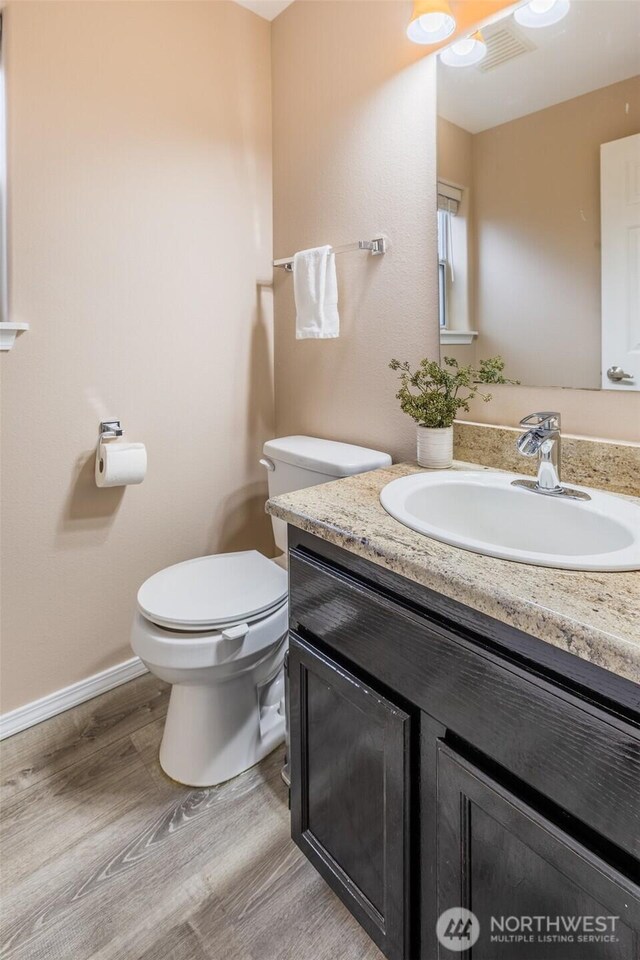 half bath featuring visible vents, baseboards, toilet, wood finished floors, and vanity