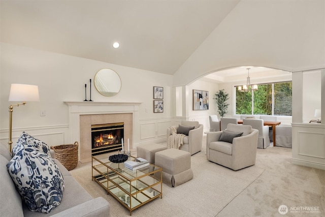 carpeted living room featuring lofted ceiling, arched walkways, a tile fireplace, a decorative wall, and a chandelier