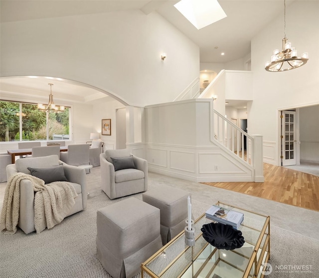 living area with a wainscoted wall, stairs, arched walkways, a notable chandelier, and a decorative wall