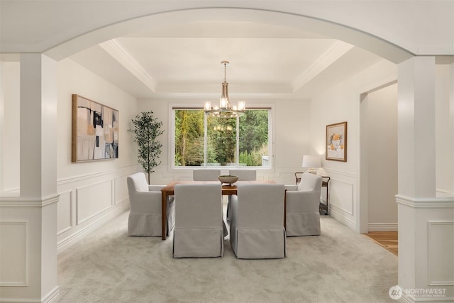 dining room with a raised ceiling, arched walkways, and light carpet