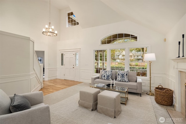 living room featuring a wainscoted wall, a high end fireplace, vaulted ceiling, a decorative wall, and a chandelier