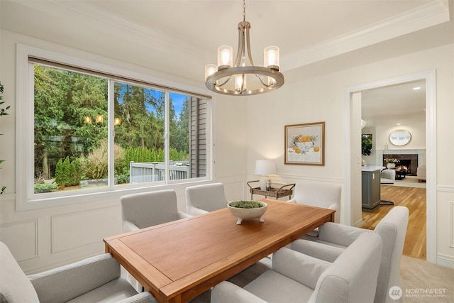 dining space featuring light wood-style floors, a lit fireplace, ornamental molding, and a decorative wall