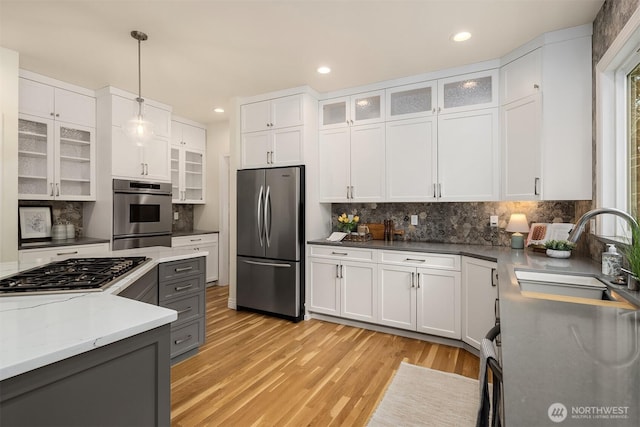 kitchen with light wood-style flooring, a sink, hanging light fixtures, white cabinets, and appliances with stainless steel finishes