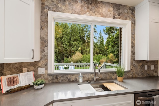 kitchen with stainless steel dishwasher, white cabinets, backsplash, and a sink