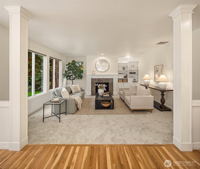 living area with visible vents, wood finished floors, a tile fireplace, and ornate columns