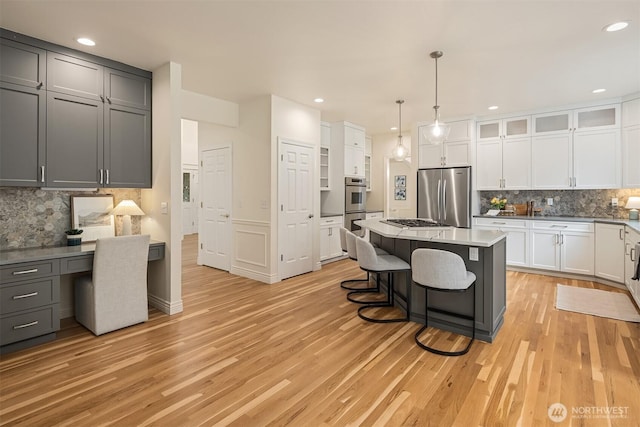 kitchen with a center island, a breakfast bar area, light wood-style flooring, appliances with stainless steel finishes, and built in study area