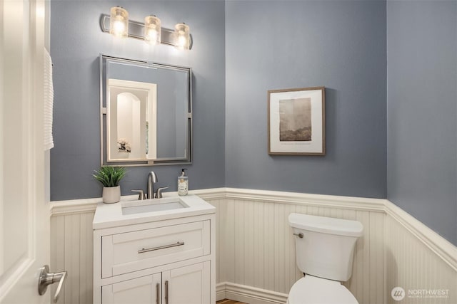 bathroom with a wainscoted wall, toilet, and vanity