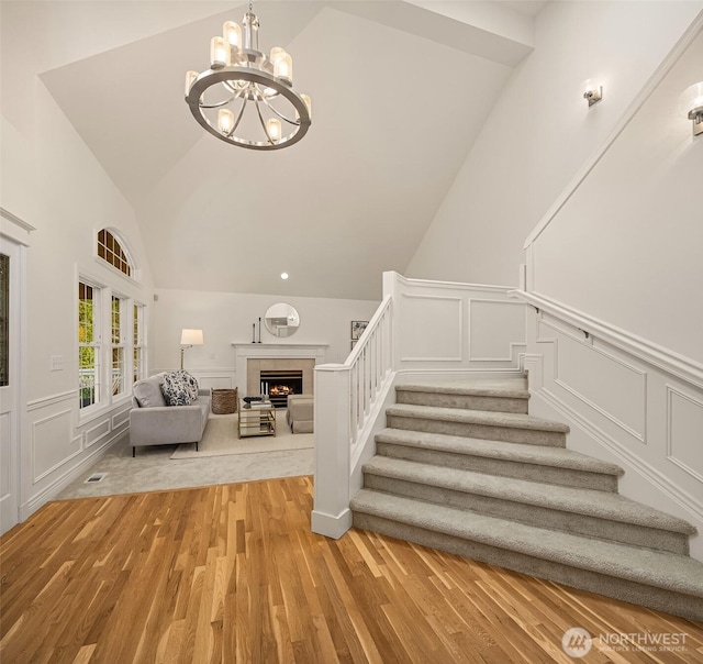 staircase with visible vents, vaulted ceiling, a warm lit fireplace, wood finished floors, and a decorative wall