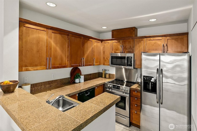 kitchen with a sink, tile counters, brown cabinetry, and stainless steel appliances