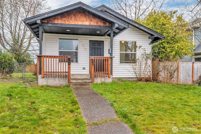 view of front of home with covered porch, a front lawn, and fence