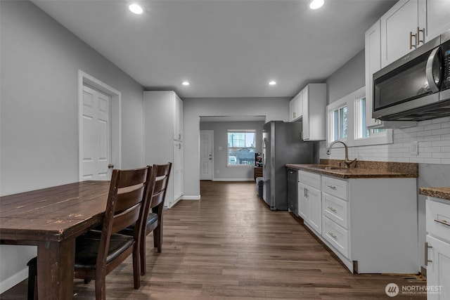kitchen featuring stainless steel microwave, a sink, dishwasher, decorative backsplash, and dark wood-style flooring
