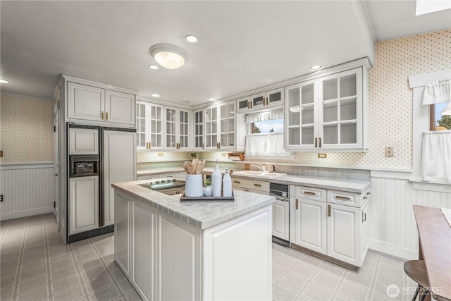 kitchen with a wainscoted wall, paneled built in refrigerator, wallpapered walls, and tile counters