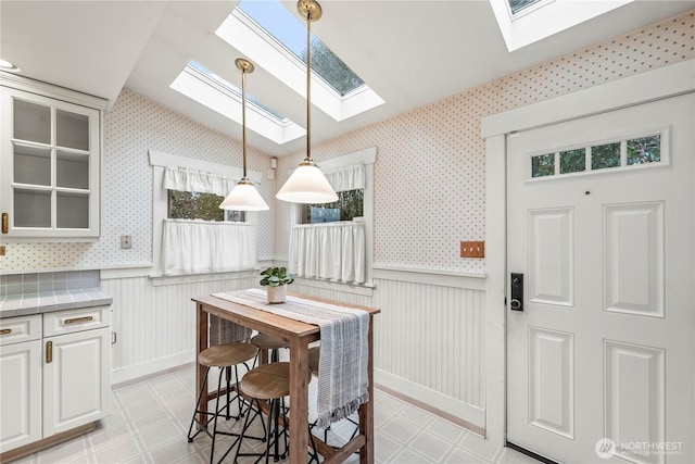 dining area featuring lofted ceiling, wainscoting, and wallpapered walls