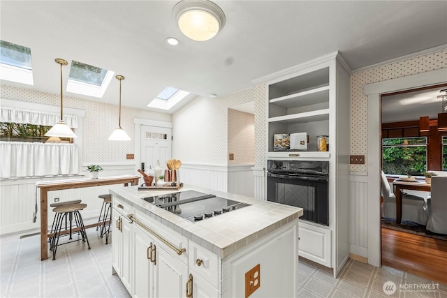 kitchen featuring wainscoting, tile countertops, black appliances, and wallpapered walls