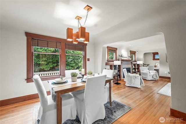 dining space with a chandelier, baseboards, light wood-style flooring, and a fireplace