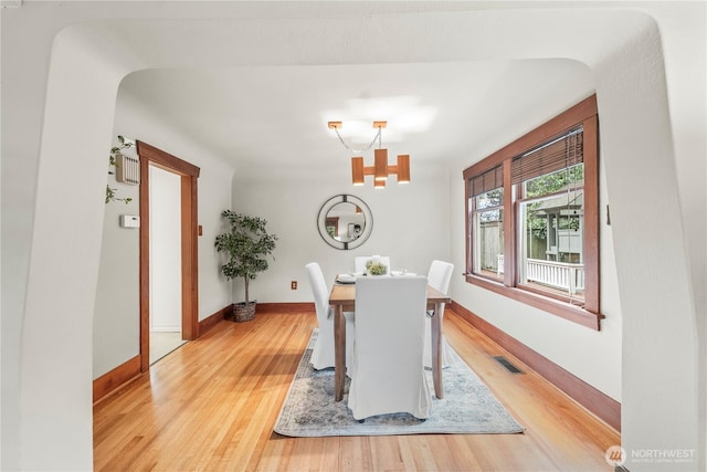 dining area with arched walkways, light wood-style floors, visible vents, and baseboards