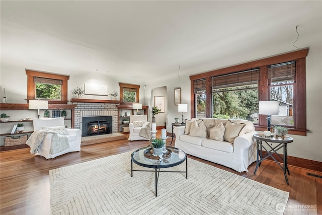 living area featuring visible vents, baseboards, a fireplace, wood finished floors, and arched walkways