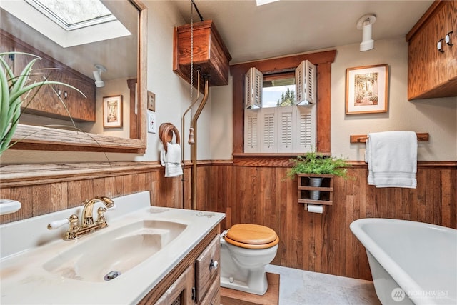 bathroom with a wainscoted wall, a soaking tub, a skylight, wood walls, and toilet