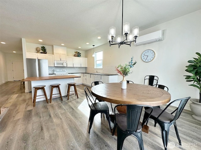 dining room featuring a wall unit AC, light wood-style flooring, recessed lighting, a textured ceiling, and a notable chandelier