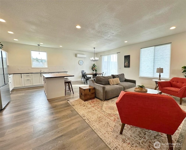 living room featuring wood finished floors, baseboards, recessed lighting, a wall mounted air conditioner, and a textured ceiling