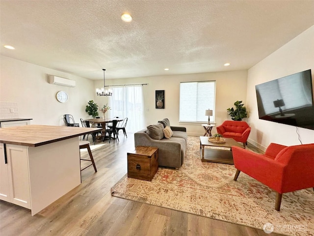 living room with light wood-style flooring, a textured ceiling, a wall unit AC, recessed lighting, and a chandelier