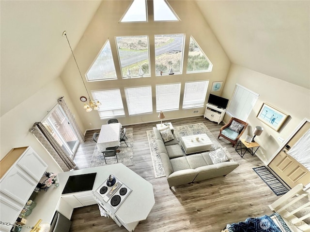 living room with baseboards, high vaulted ceiling, an inviting chandelier, and wood finished floors