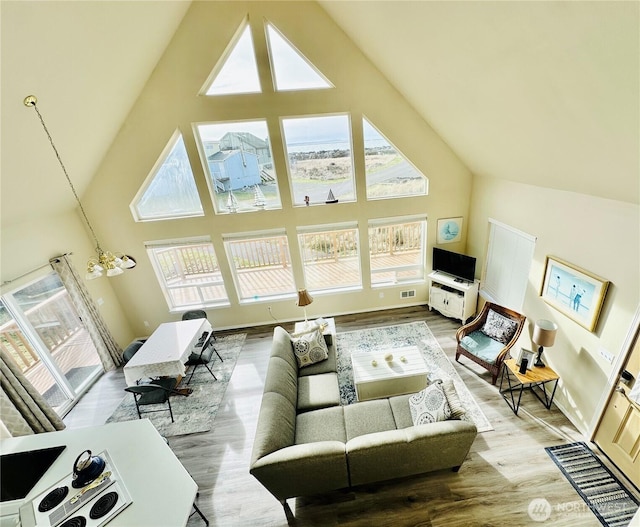 living area with wood finished floors, visible vents, a wealth of natural light, and high vaulted ceiling