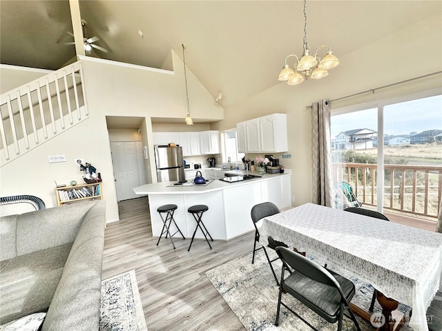 dining area featuring plenty of natural light, light wood-style flooring, high vaulted ceiling, and ceiling fan with notable chandelier