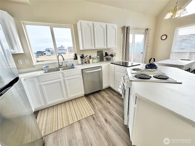 kitchen featuring vaulted ceiling, light wood-style flooring, appliances with stainless steel finishes, white cabinets, and a sink